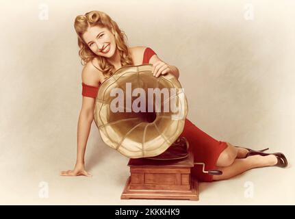 Attractive retro 60s pin up girl smiling beside vintage record phonograph music player holding large brass horn in a depiction of old classic audio Stock Photo