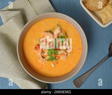Healthy spicy Thai prawn soup with crackers on blue background in horizontal format shot from above. Stock Photo