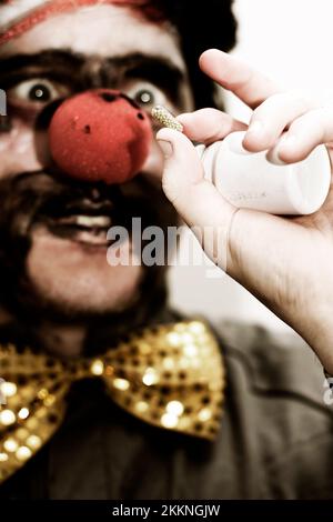 Darkened Image Of A Clown Holding Up A Prescribed Medication Tablet To Help Bring His Humor Back Stock Photo