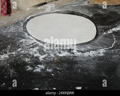 The chef rolling pizza dough into a flatten circle shape by wooden rolling pin with flour on black background Stock Photo