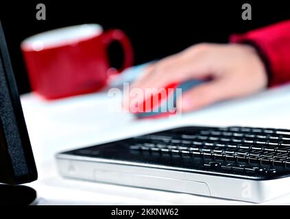 A lady in red blouse is using her wireless mouse at a computer workstation. She is working at home. Shallow D.O.F Stock Photo