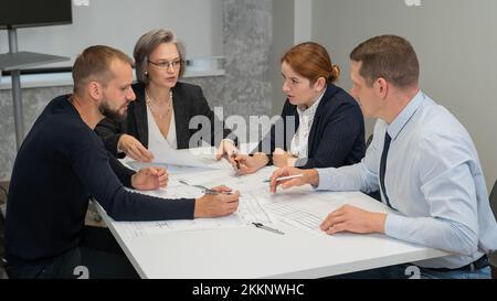 Four colleagues are discussing blueprints in a conference room in an office. Brainstorming of engineers and architects. Stock Photo