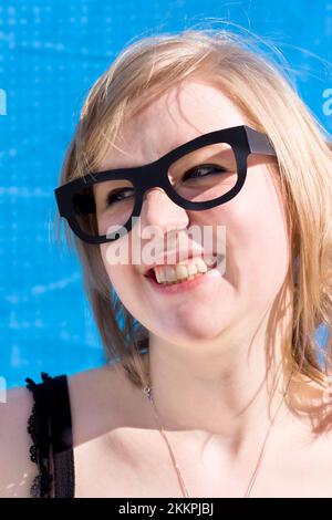Mischievous Looking Woman Beams In A Cheeky Grin Expression While Wearing Fake Glasses In Front Of A Blue Background Stock Photo