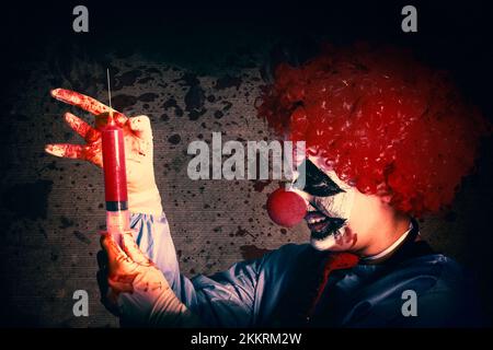 Scary clown holding large injection needle filled with human vaccine test trials. Bad medicine Stock Photo