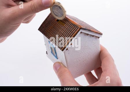 Hand dropping coin into the moneybox in the shape of a model house Stock Photo