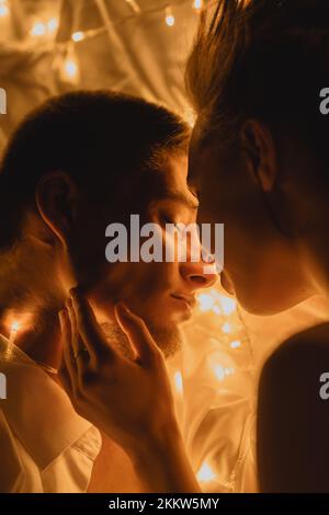 Nice couple in love kissing celebrating new year or Christmas in decorated with garland room. Silhouette of a loving couple hugging. Bokeh effect of g Stock Photo