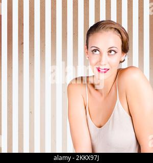 Beautiful elegant fashion model with set fifties brunette hairstyle wearing chic make-up thinking on striped beige background Stock Photo