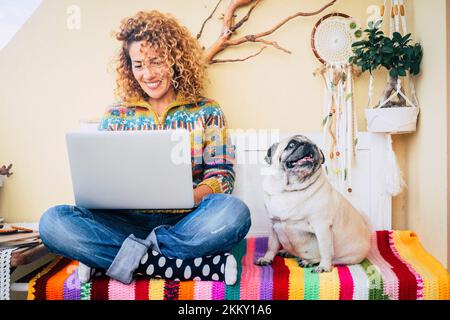 One happy woman using laptop outdoor at home sitting near her best friend dog pug and enjoying technology and friendship. Cheerful attractive female w Stock Photo