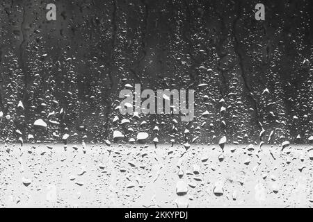 Rain drops close up on window glass outdoors.  Texture of water in heavy rain. Gloomy autumn  morning. Monochrome natural background Stock Photo