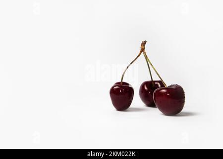 Three red cherries with stems on white background Stock Photo