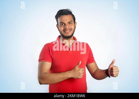 Young Indian Man Doing Happy Thumbs Up Gesture With Hand, Approving Expression Looking At The Camera Showing Success Stock Photo