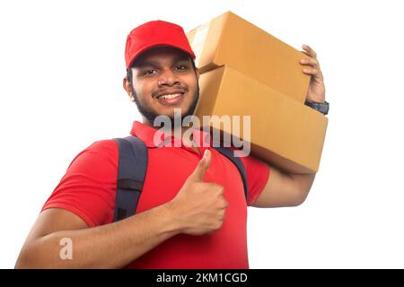 Portrait Of Young Delivery Man Carrying Cardboard Box On Shoulder and showing his thumb up Stock Photo