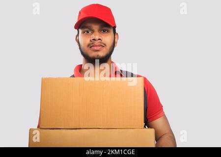 Portrait Of Young Delivery Man Holding Cardboard Box Against Grey Background Stock Photo