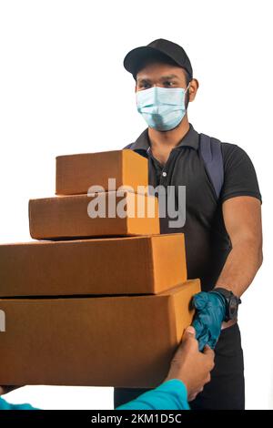 Happy young indian delivery man in black uniform, medical face mask, protective gloves carry cardboard box in hands Stock Photo