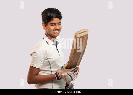 A boy in cricket uniform holding Cricket Bat looking into bat Stock Photo