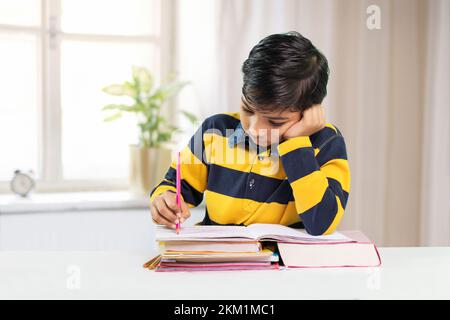 Indian boy student doing study at home, He is writing on notebook and doing his homework Stock Photo