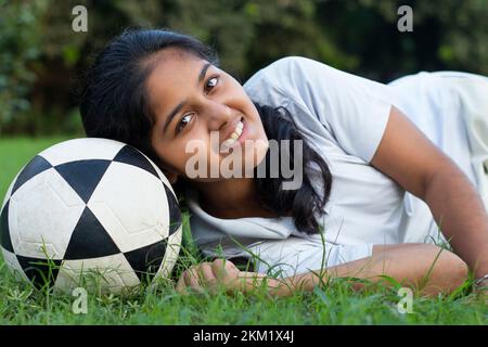 Portrait of smiling girl lying on a meadow with head on soccer ball Stock Photo