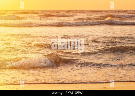 Sunset above sea. Natural sunrise sky warm colors over ripple sea with small waves. Ocean water foam splash washing sandy beach at sunset Stock Photo