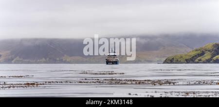 Expedition ship standing in the bay off South Georgia  of Leith Harbour - old, abandoned and largest of all seven whaling stations on South Georgia. Stock Photo