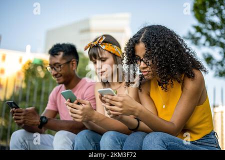 Three young people looking at cell phone, diverse friends spending time on social network Stock Photo