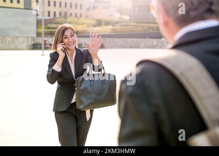 Mature business woman using smartphone during a call meets with her colleague in front of office, sun light effect Stock Photo