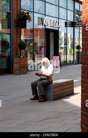 Man reading on a bench in the Old Market shopping centre, Hereford, Herefordshire Stock Photo