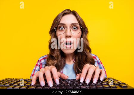 Portrait of excited speechless woman curly hairstyle checkered shirt typing keyboard impressed looking isolated on yellow color background Stock Photo