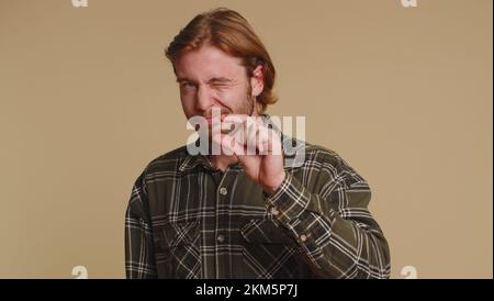 Need some more, please give me. Man showing a little bit gesture with sceptic smile, showing minimum sign, measuring small size, asking for help. Young guy isolated alone on beige studio background Stock Photo