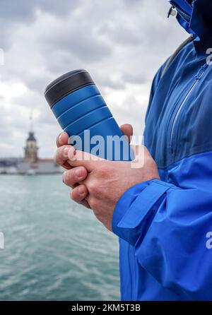 Blue jacket man holding thermos flask with a seascape in the background. Winter time in Istanbul. Stock Photo