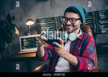 Photo of funny positive freelancer wear hat glasses headphones watching video modern device indoors workplace workstation loft Stock Photo
