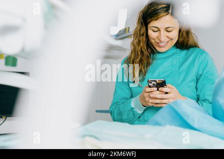 Smiling dentist in the operating room uses mobile phone Stock Photo