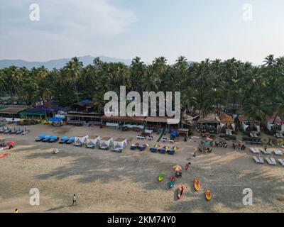 A beautiful view of people relaxing on Palolem Beach with huts and palm trees in South Goa Stock Photo