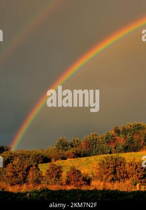 A double rainbow above a sunlit hillside in autumn. Stock Photo