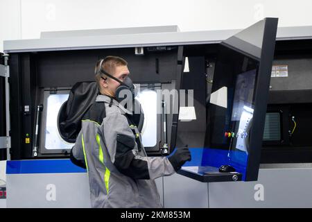 The worker controls workflow inside large industrial 3D printer printing metal powder standing near worker's control panel. The working process. Industrial powder 3d printer for metal and worker man. Stock Photo