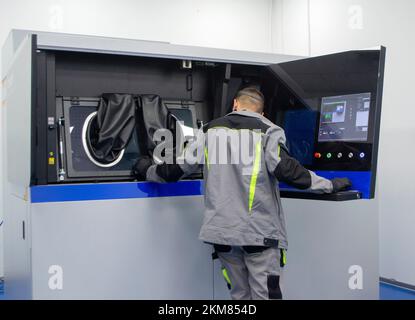 The worker controls workflow inside large industrial 3D printer printing metal powder standing near worker's control panel. The working process. Industrial powder 3d printer for metal and worker man. Stock Photo