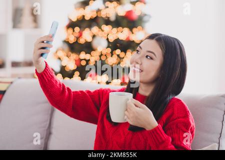 Portrait of beautiful nice positive charming woman with straight hairdo wear red knit pullover hold cup making selfie in house indoors Stock Photo