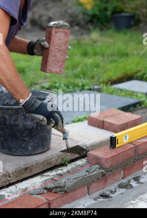 Construction work in progress. Male builder working with red bricks. Masonry wall close up photo. Stock Photo