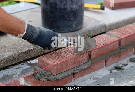 Construction work in progress. Male builder working with red bricks. Masonry wall close up photo. Stock Photo