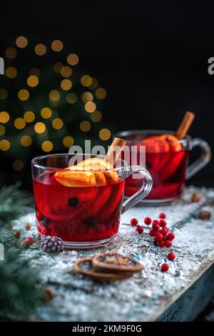 Mulled wine, hot punch or berry tea with slices of orange and cinnamon in transparent mugs on a snow-covered table. Stock Photo
