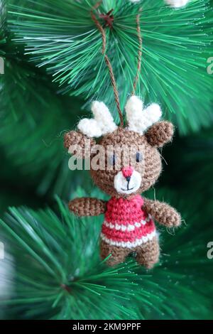 Crochet Christmas decoration on a tree. Cute amigurumi toy on a green Christmas tree. Stock Photo