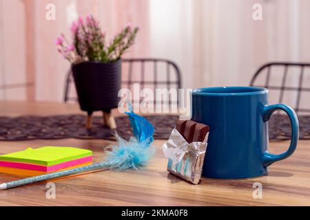Coffee mug and chocolate on wooden table, colorful note papers. Side view, copy space, close-up. Kitchen dining table, break concept Stock Photo
