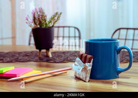 Coffee mug and chocolate on wooden table, colorful note papers. Side view, copy space, close-up. Kitchen dining table, break concept Stock Photo