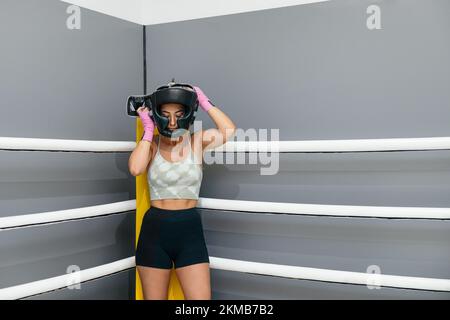 Young woman putting protective headgear for practicing boxing standing in ring boxing Stock Photo