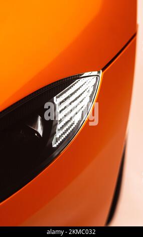 A vertical closeup of an Aston Martin Vantage crystal headlight in Golden Saffron background Stock Photo