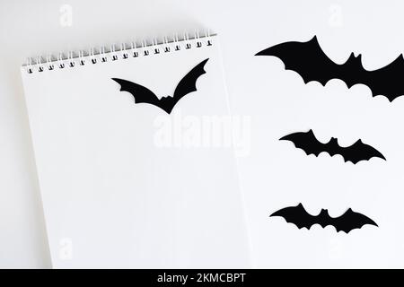 Blank notepad on white background with paper bats silhouettes, traditional Halloween decor. The concept of planning and organizing autumn holidays, Ha Stock Photo