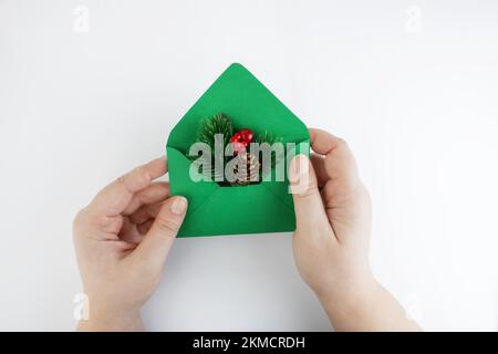 Green envelope with a Christmas branch in female hands on a white background. Christmas mail or gifts. Concept for congratulations for Christmas or Ne Stock Photo