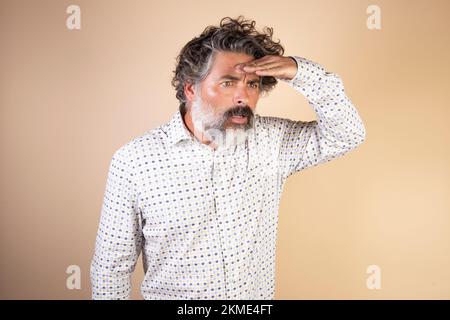 A middle-aged man looking away with his hand on head isolated on a beige background. A search concept. Stock Photo