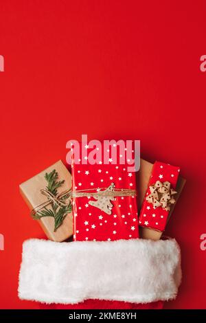 Santa Claus hat with gift boxes on red background. Christmas presents and santa hat on red background. Xmas gift ideas Stock Photo