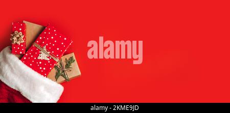 Santa Claus hat with gift boxes on red background. Christmas presents and santa hat on red background. Xmas gift ideas Stock Photo