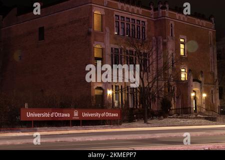 Traffic, light trails pass by a pedestrian level sign for the University of Ottawa, uOttawa in the downtown Ottawa, Canada's capital city. Stock Photo